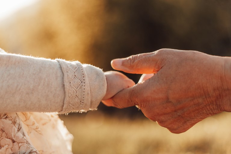 Eine Kinderhand hält die Hand eines Erwachsenen im Abendlicht