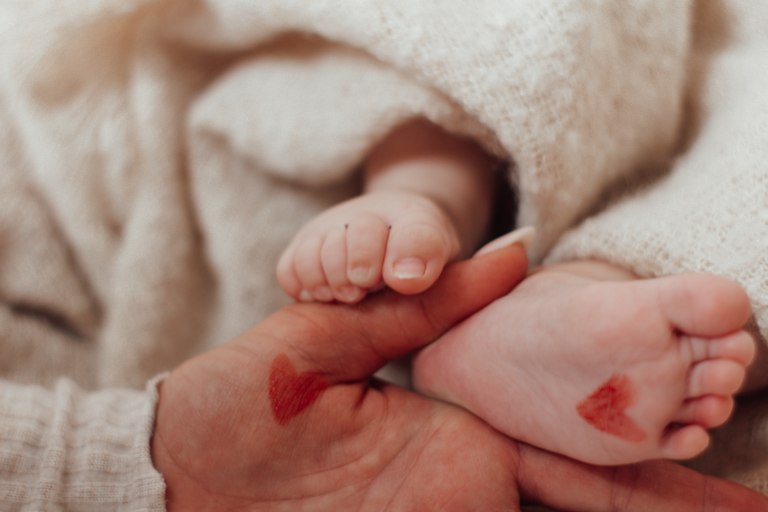 Kleine Babyfüße in den Händen eines Erwachsenen